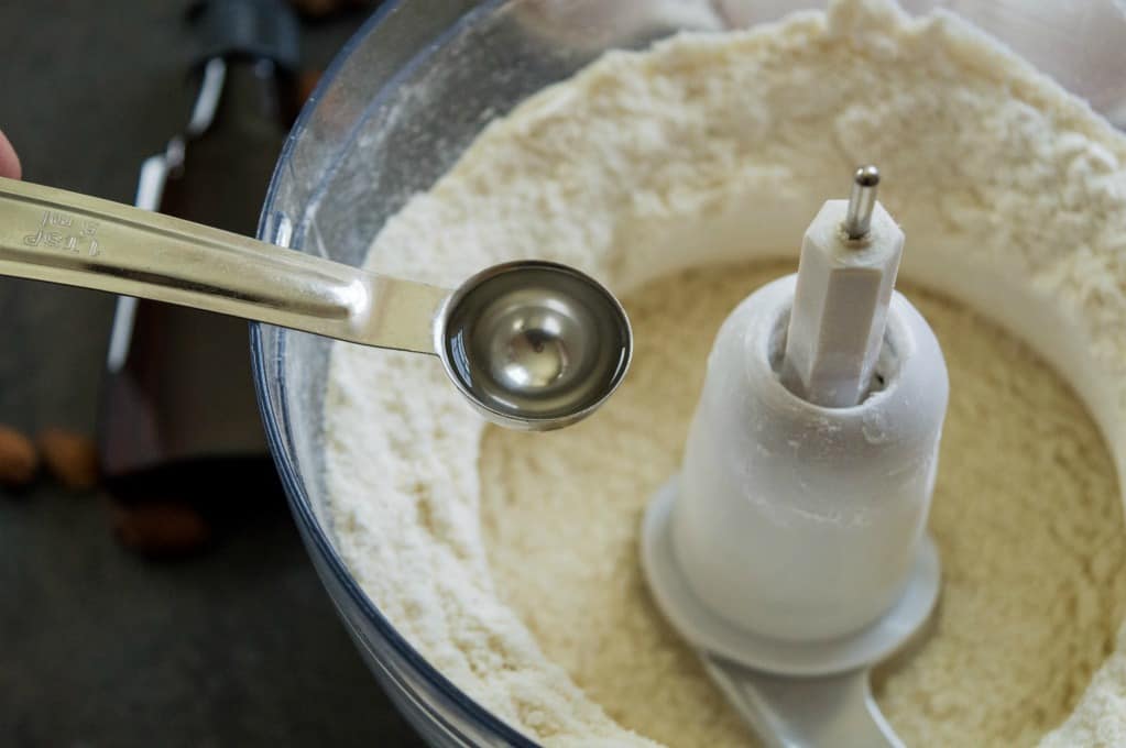 adding the almond extract to the food processor with the almond flour and powdered sugar