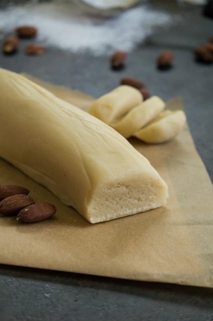 Homemade Almond Paste log on a piece of brown parchment paper with whole almonds around it. 