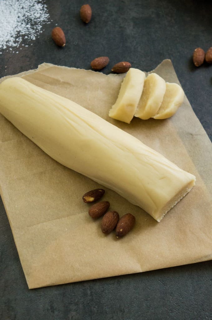 Overhead shot of the almond paste log on piece of brown parchment paper on dark background. 