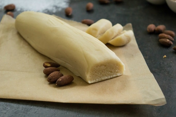 log of homemade almond paste on parchment paper with roasted almonds
