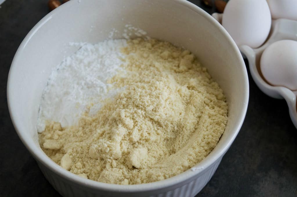 bowl of almond flour and powdered sugar with eggs in the background