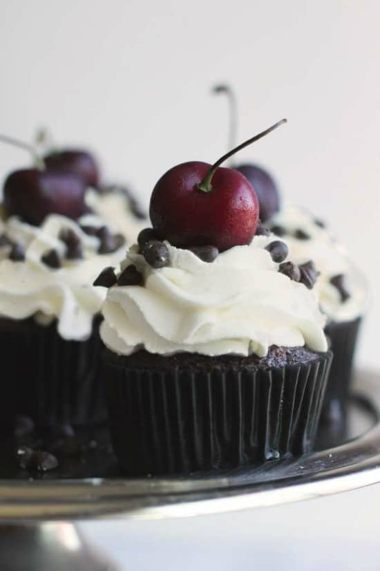 Chocolate cupcakes studded with chopped cherries and topped with fresh whipped cream and more chocolate. #cupcakes #chocolate #chocolatecupcakes #blackforest #germancake #cupcakerecipe 