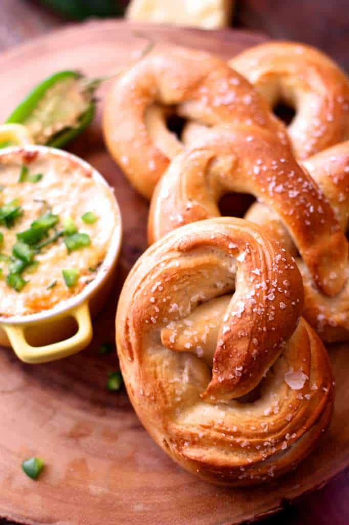 Overhead shot of pretzels next to a dish of beer cheese on wood cutting board. 