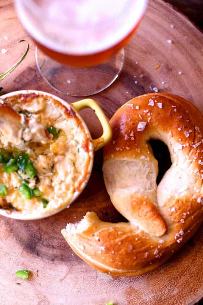 half a pretzel next to a small yellow dish of beer cheese