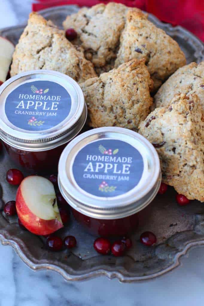 Jars of the labeled jam on a silver plate with a bunch of scones around it. 