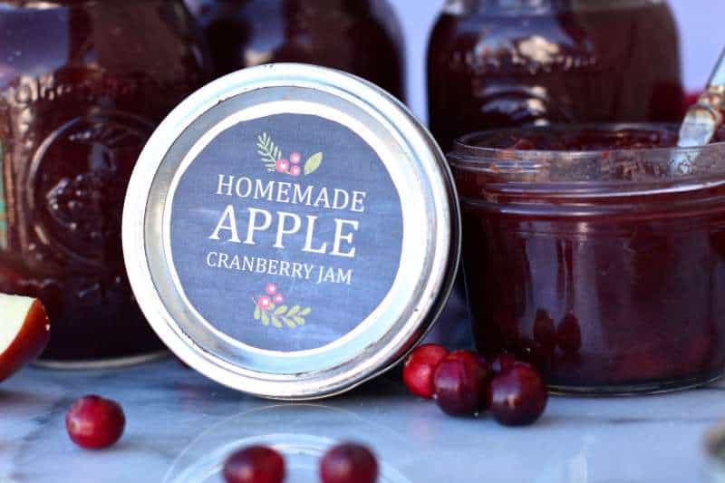 Jam lid with cute cranberry apple label and jars of jam next to it.