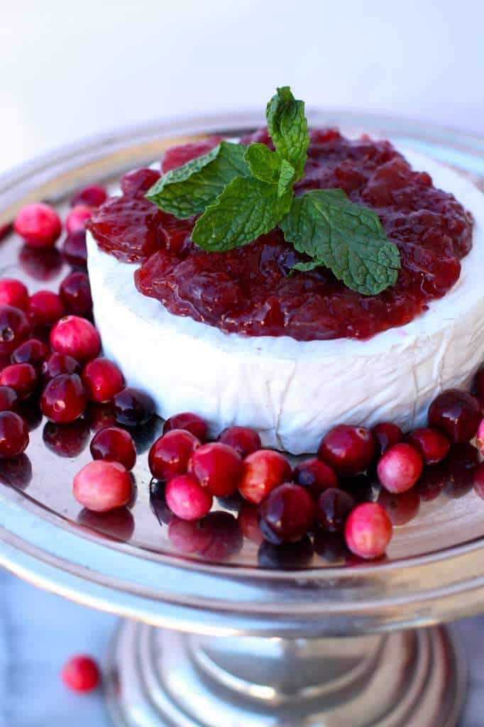 Silver cake plate with a round of brie that is topped with the jam and mint leaves. 
