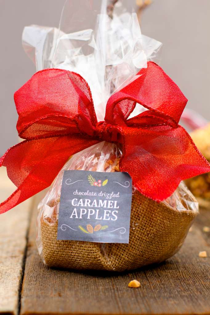 Caramel apple in bag with large red bow on wood surface. 