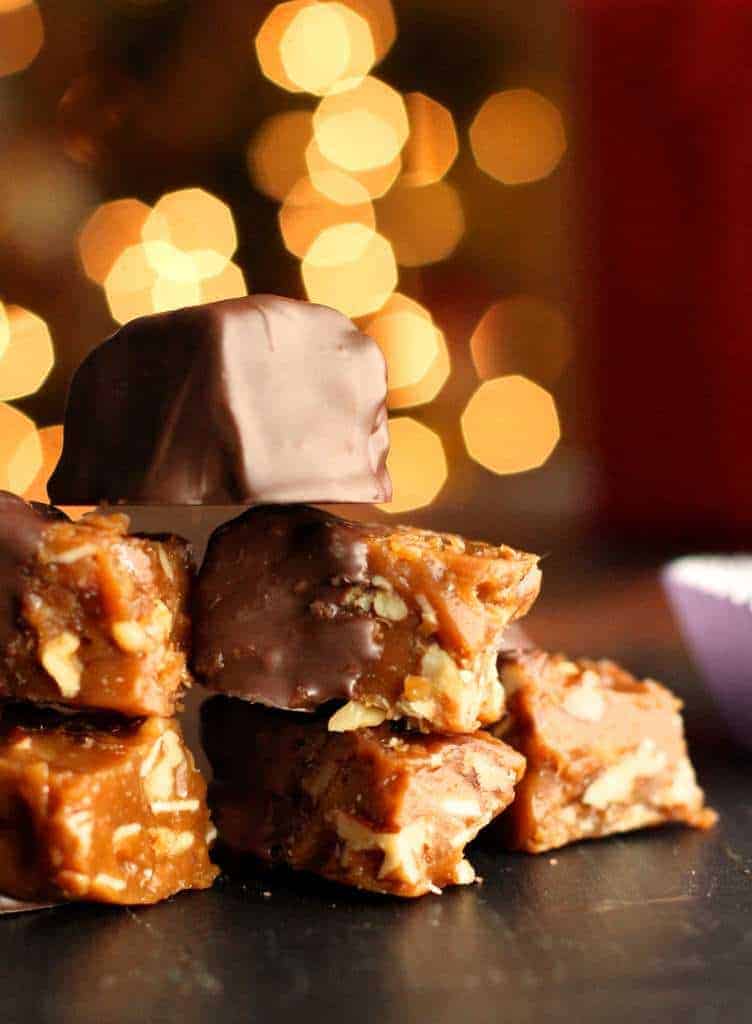 Pieces of California brittle that have been half dipped in chocolate stacked with Christmas lights in background. 