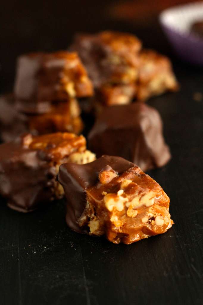California brittle half covered in chocolate showing the layers of hard caramel and mixed nuts. 