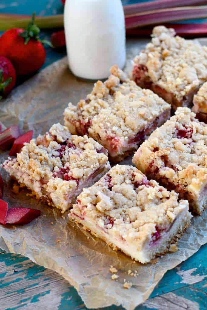 several strawberry rhubarb sugar cookie bars sitting on a piece of brown parchment paper with glass of milk in background