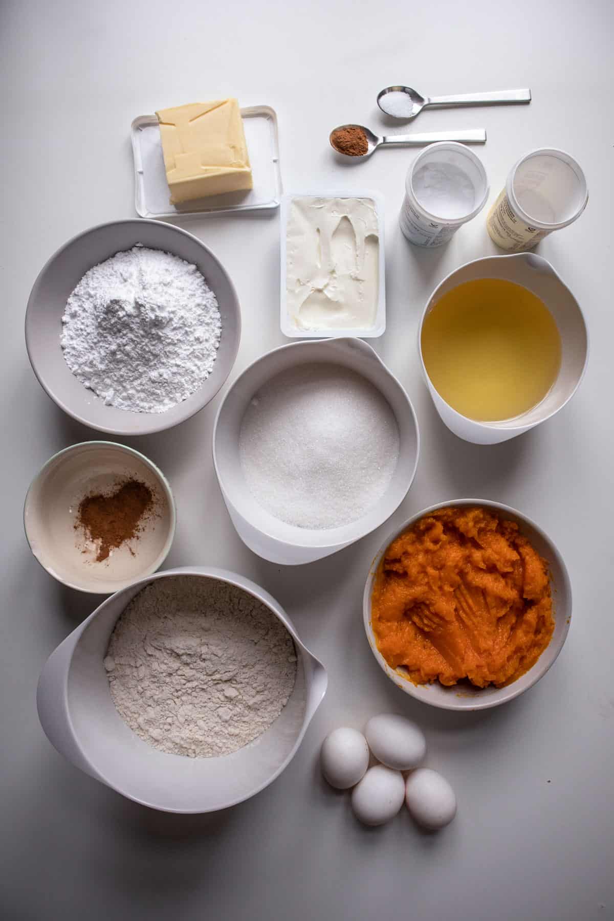 Ingredients to make the pumpkin snickerdoodle cupcakes in white bowls on white background.