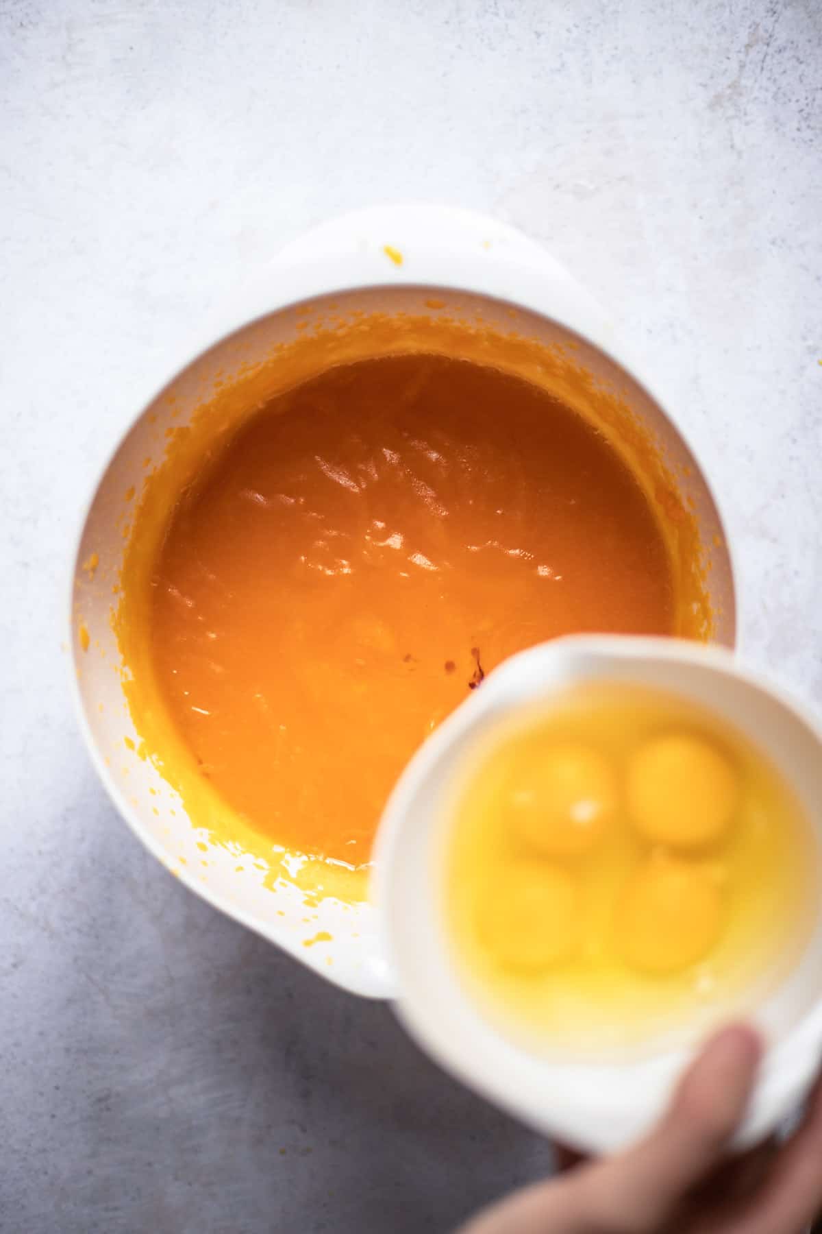 Adding the small bowl of eggs to the pumpkin mixture in white bowl.