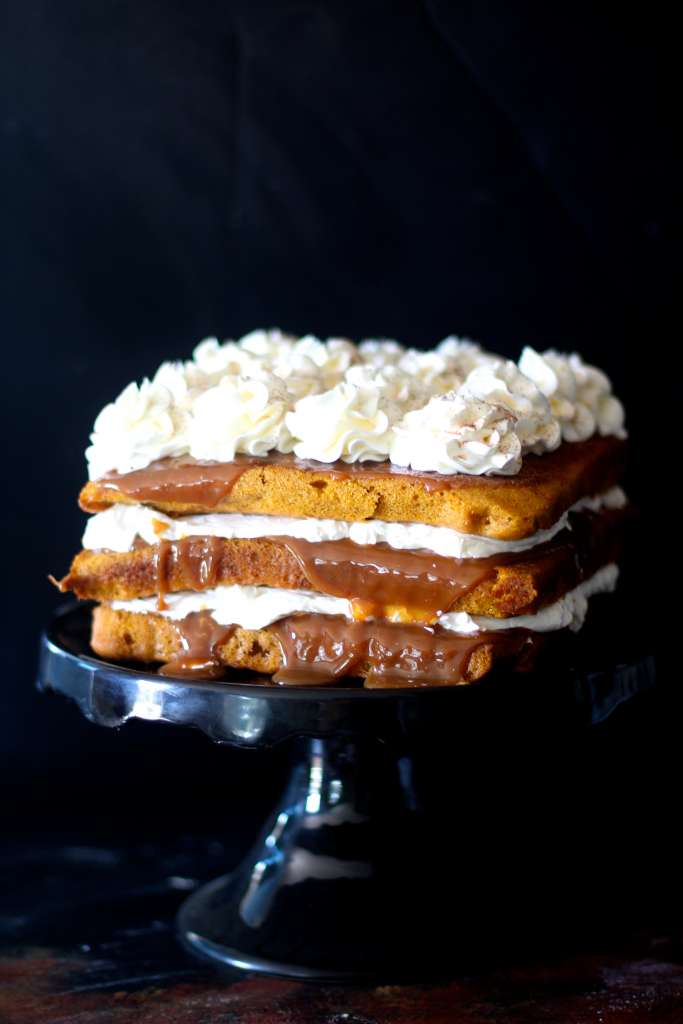 Square pumpkin cake with dulce de leche oozing out and piped cream cheese frosting on black cake plate. 