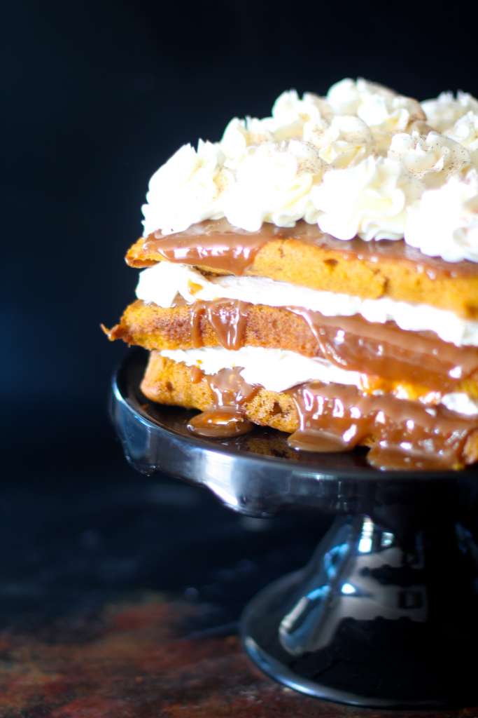 Side shot of the 3 layer cake on a black cake plate on a black background. 