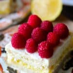 Square slice of Lemon Cheesecake Bars on decorative plate with fresh raspberries on top