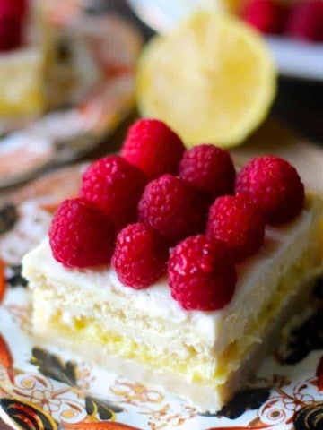 Square slice of Lemon Cheesecake Bars on decorative plate with fresh raspberries on top