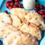 several hand pies on a blue plate next to cherries and a glass of milk