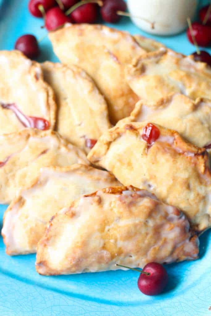 closeup of hand pies on a blue plate with cherries scattered around