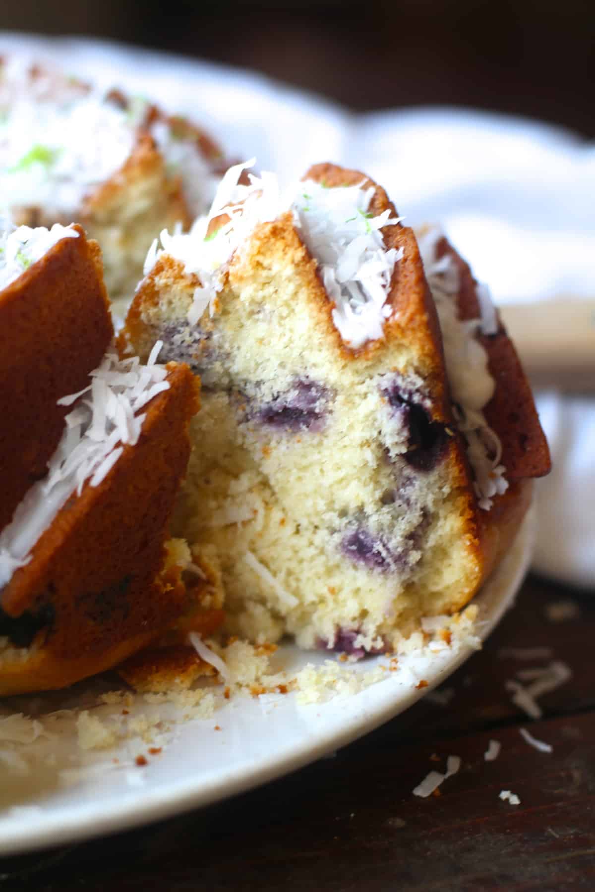 A slice of Blueberry Coconut Lime Bundt Cake showing the blueberry center on white plate. 