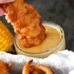 copycat chili's chicken crispers being dipped by a hand in small bowl of honey mustard sauce