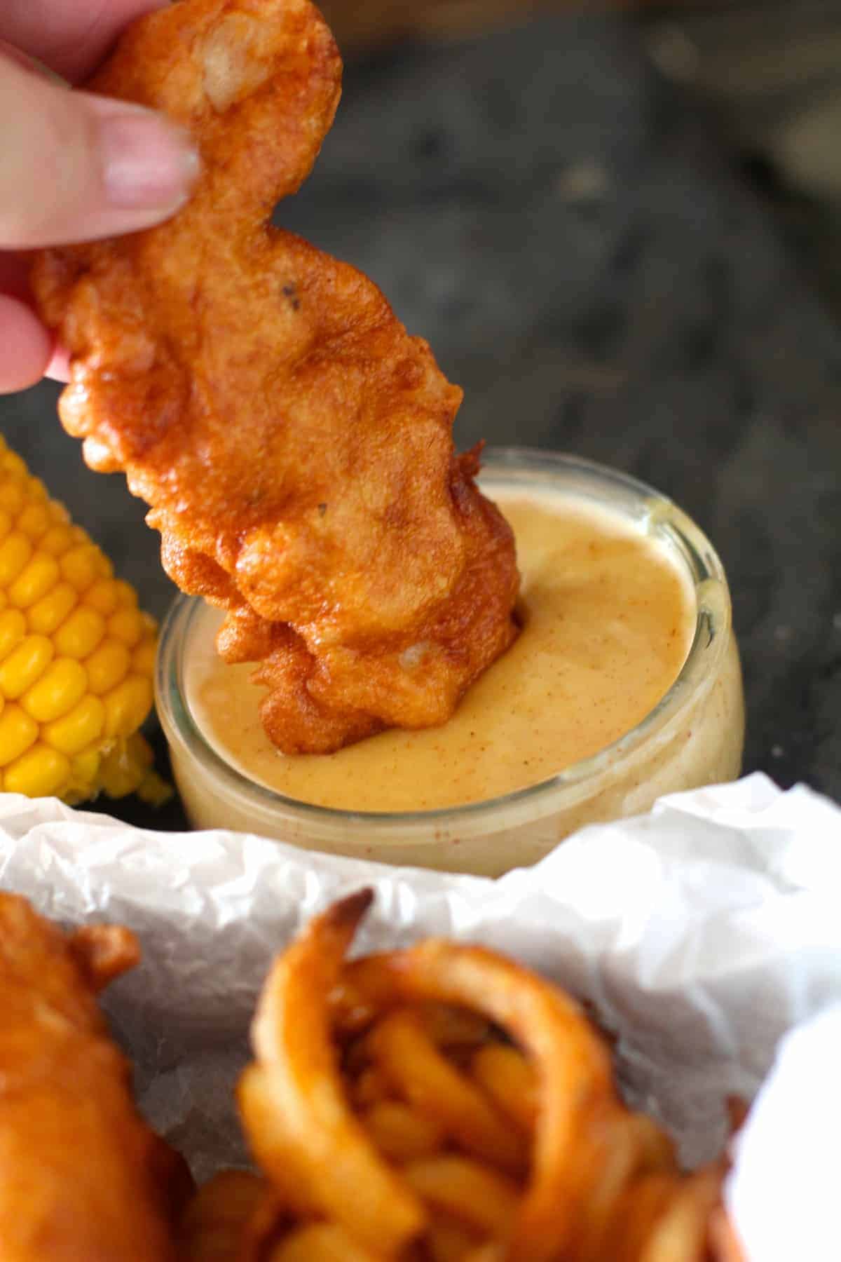 hand dipping copycat chili's chicken crispers in a small container of honey mustard sauce