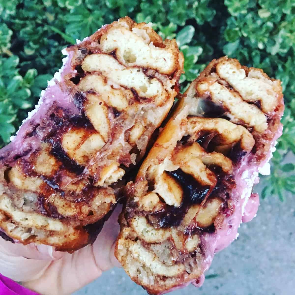 A deep fried cinnamon roll with boysenberry cream cheese frosting