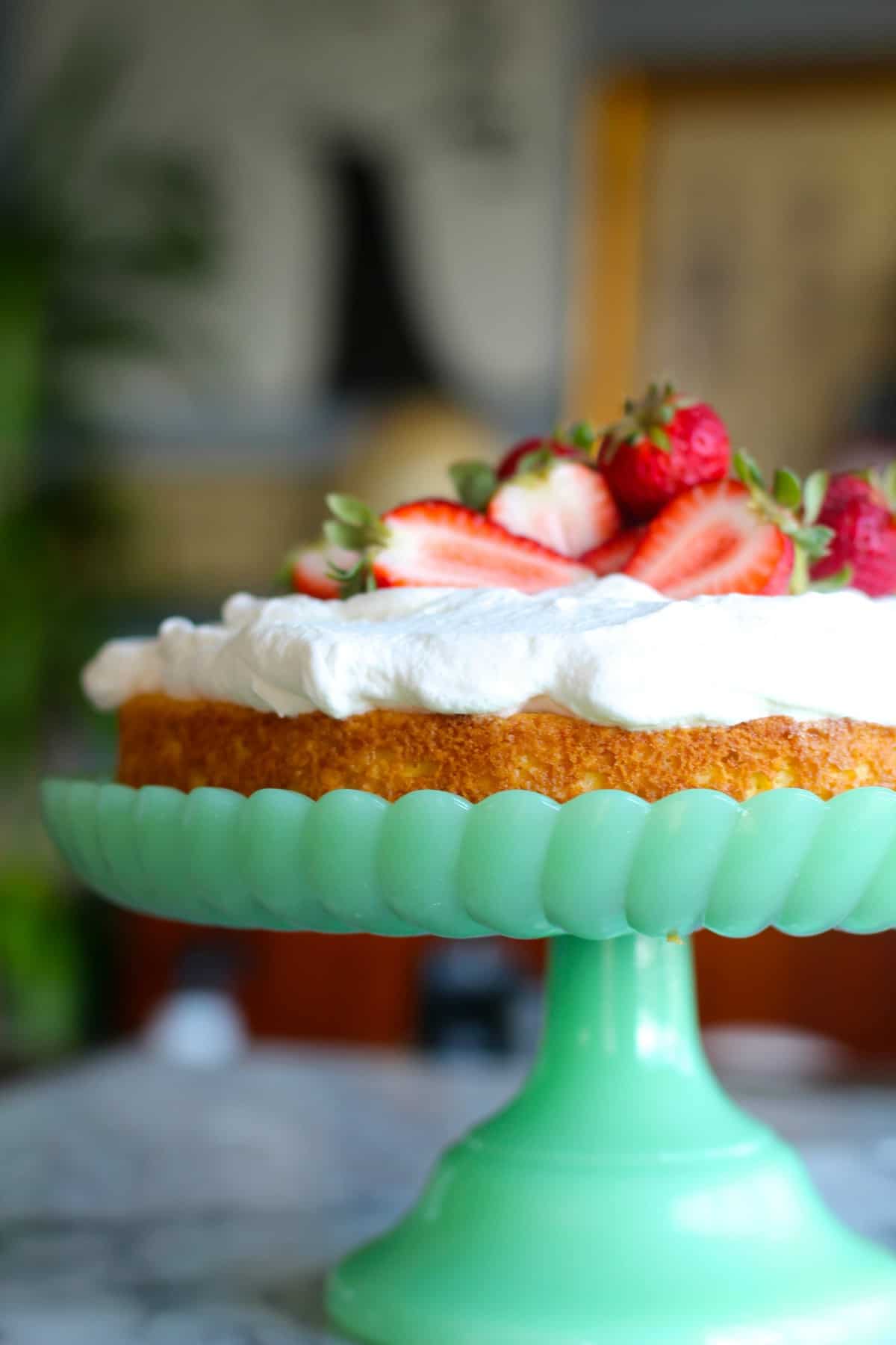 easy tres leches cake on a green cake stand with strawberries on top