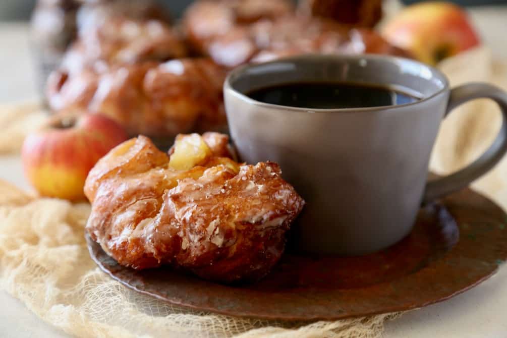 apple fritter donut on a copper plate with a cup of coffee.