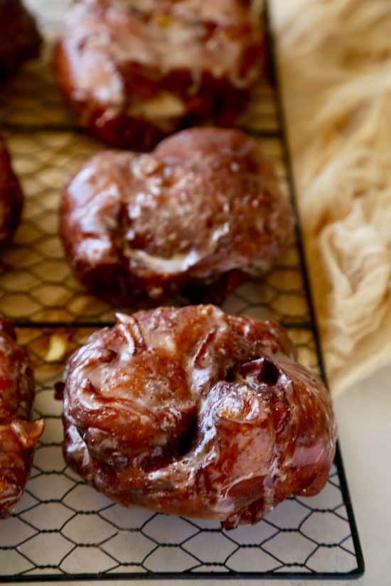 Black wire cooling rack with Apple Fritters on beige background.