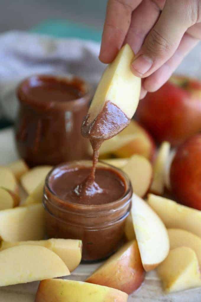 apple slice being dipped in a jar of homemade nutella surrounded by apple slices