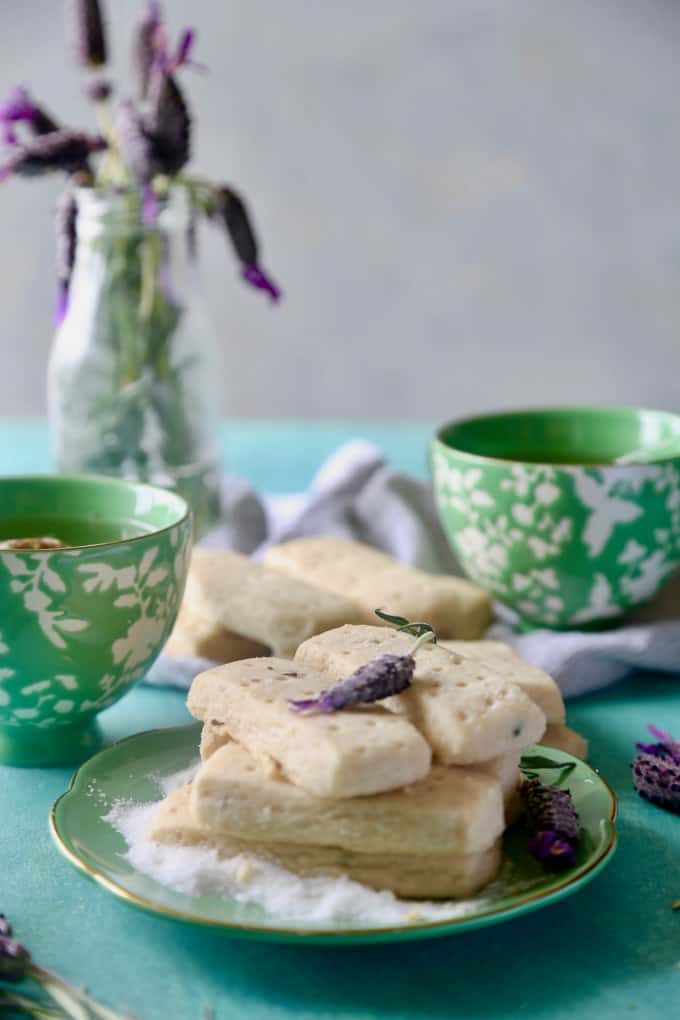 green plate of lavender shortbread cookies with 2 cups of tea in the background