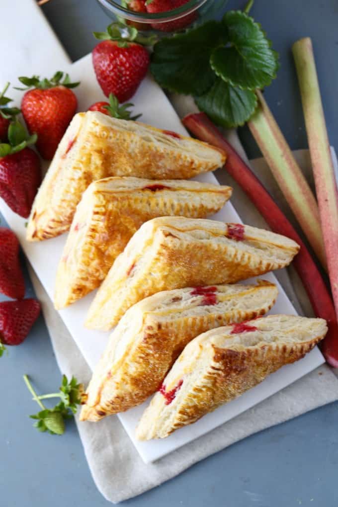 Overhead shot of the turnovers on white marble plate with strawberries and rhubarb.