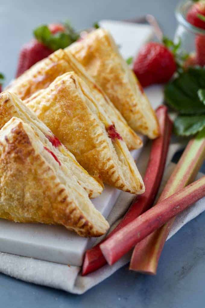 Strawberry Rhubarb Turnovers on a white marble board with fresh strawberries around it. 