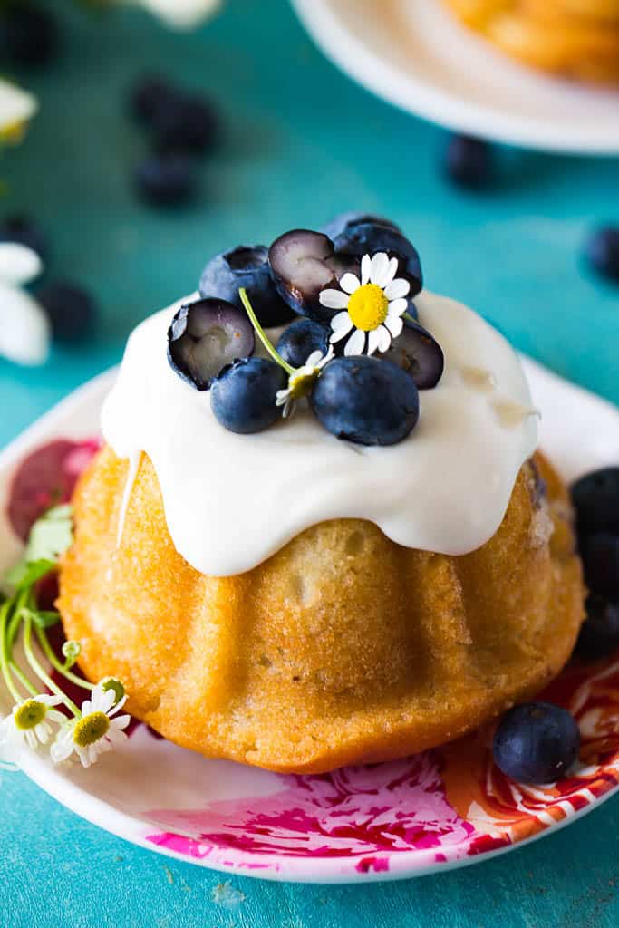 closeup of single mini blueberry bundt cakes with fresh blueberries and cream on top