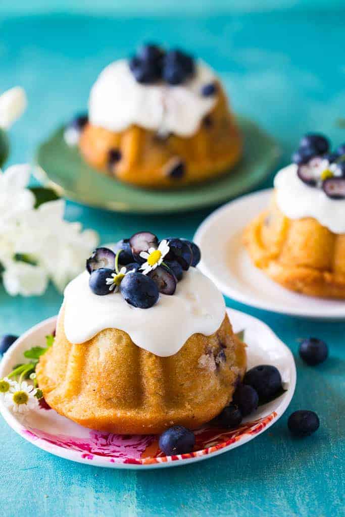 closeup of mini blueberry bundt cakes on a white platter in front of two other cakes