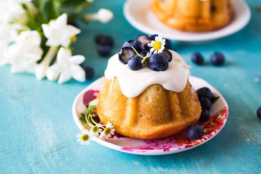 horizontal view of mini blueberry bundt cakes on a pink and white plate on a blue countertop