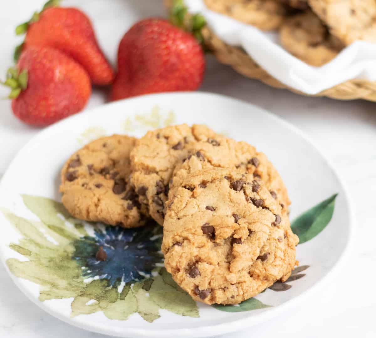 four chocolate chip strawberry cookies on a plate with three strawberries in the background