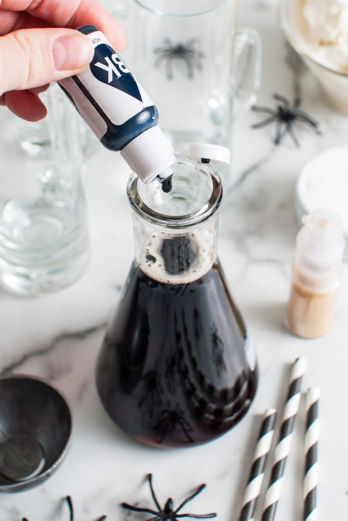 Adding drops of black food dye to the beaker of root beer. 