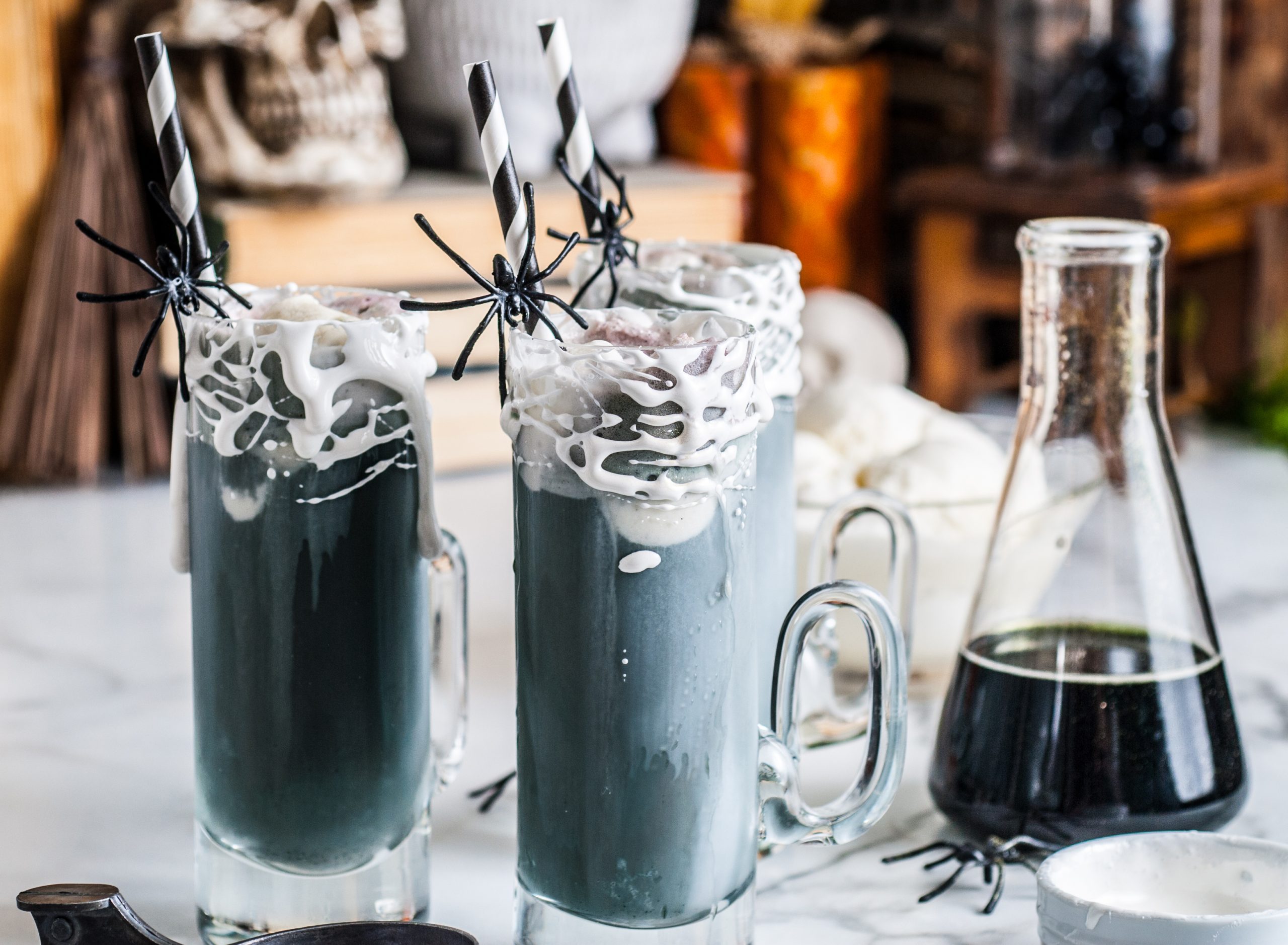 Two halloween root beer floats with beaker of black liquid off to the side. 