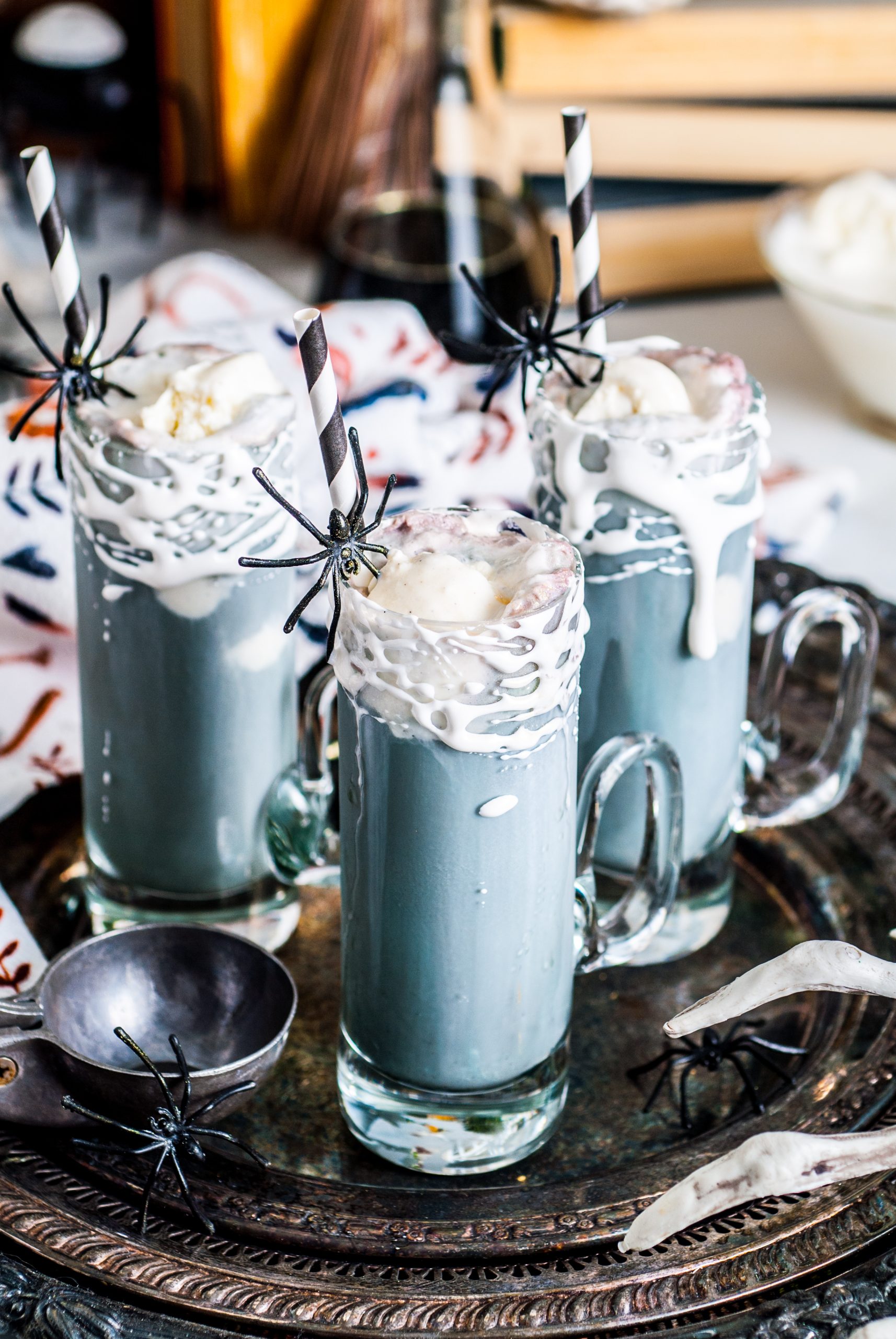 Three halloween root beer floats on a black serving tray with plastic spiders. 