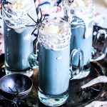 Square image of three black root beer floats with straws and plastic spiders.