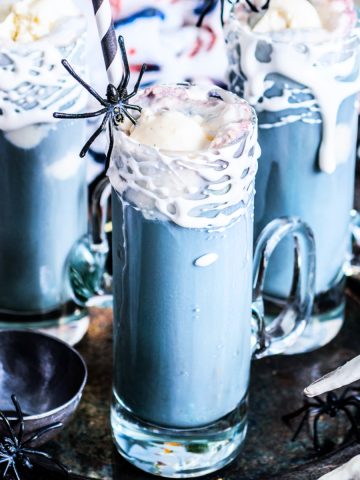 Square image of three black root beer floats with straws and plastic spiders.