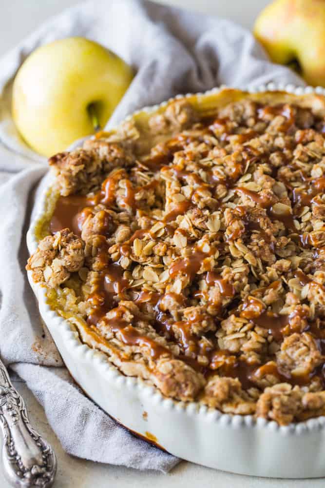 Apple Buttermilk Pie in white deep dish pie pan with apples in background. 