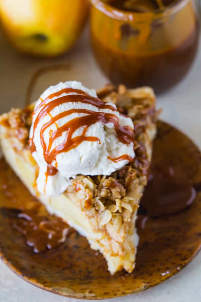 Warm slice of apple buttermilk pie with ice cream and caramel drizzle on wood plate