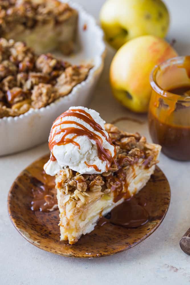 Slice of apple buttermilk pie with ice cream and caramel sauce on wood plate. 