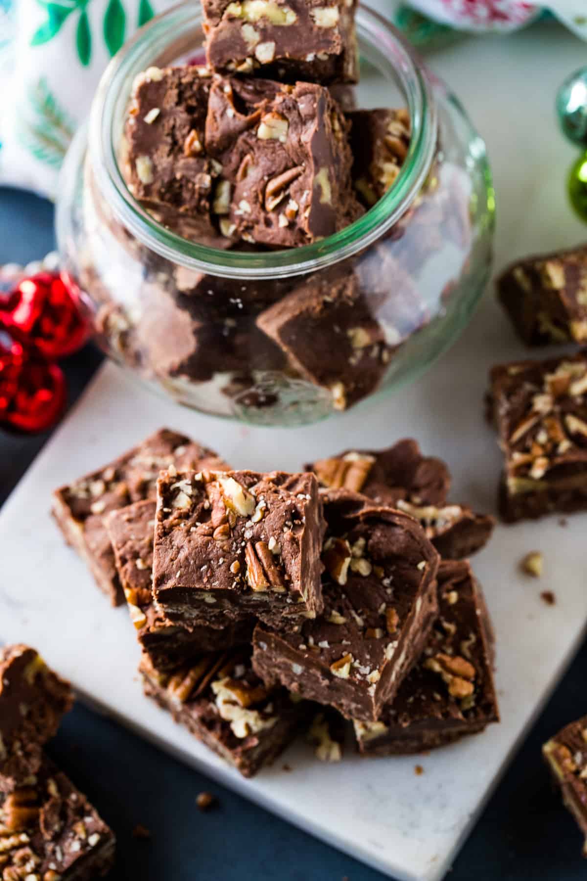 Classic Pecan Fudge stacked on marble tray with red and green ornaments around it. 