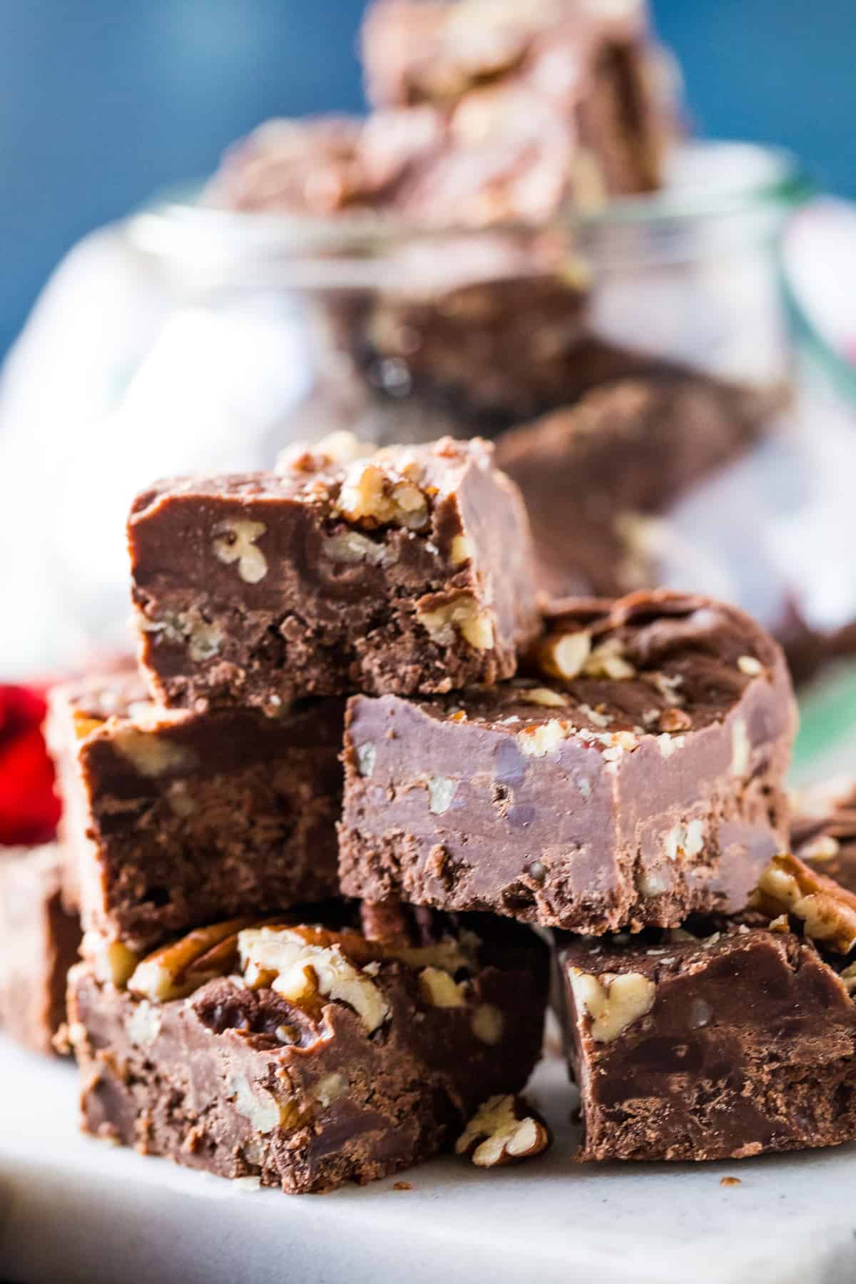 Stacked squares of pecan fudge topped with pecans on a metal tray. 