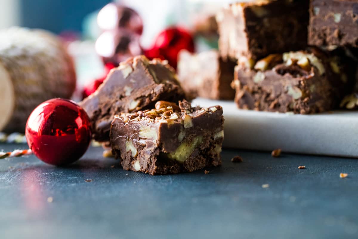 Close up shot of pecan fudge squares stacked with red Christmas ornaments next to it. 