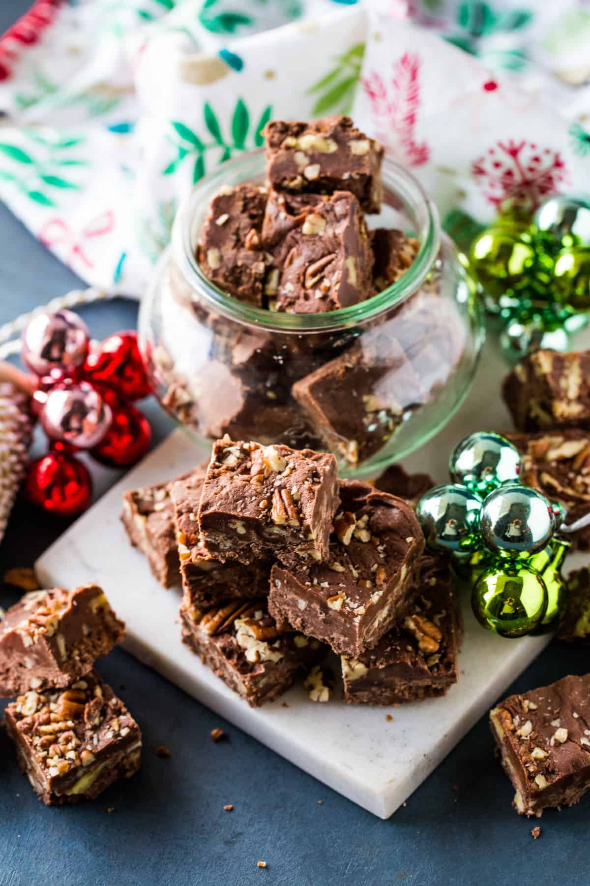 Classic Pecan Fudge squares in a glass jar and stacked on a marble board.